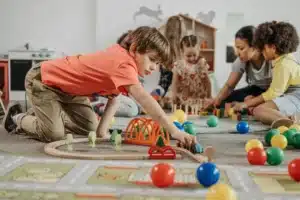 Clichés sur les assistantes maternelles. Des enfants jouent avec des jouets en bois et des balles colorées, encadrés par une assistante maternelle attentive.