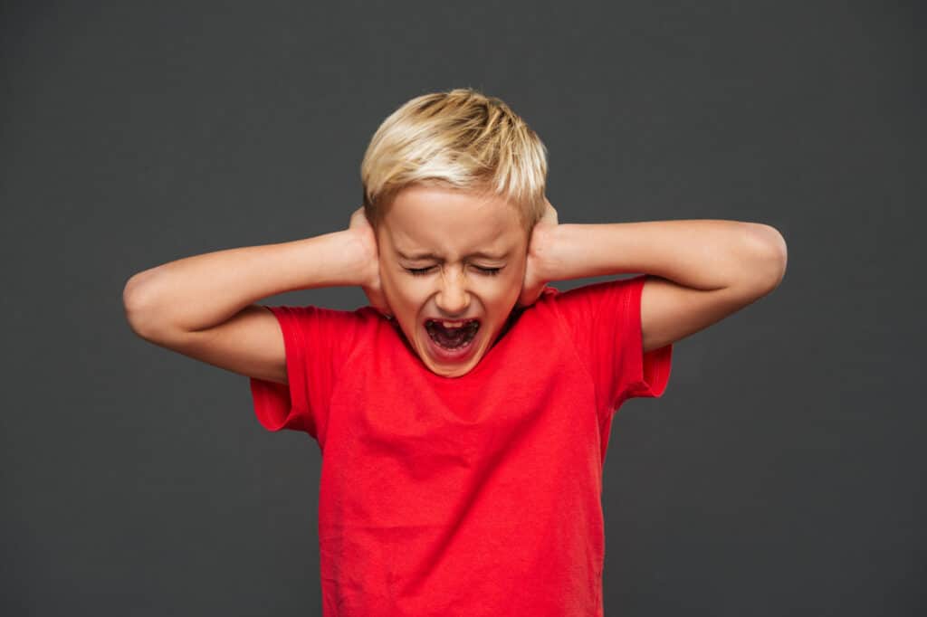 Enfant en colère se bouchant les oreilles en raison d'une surcharge sensorielle