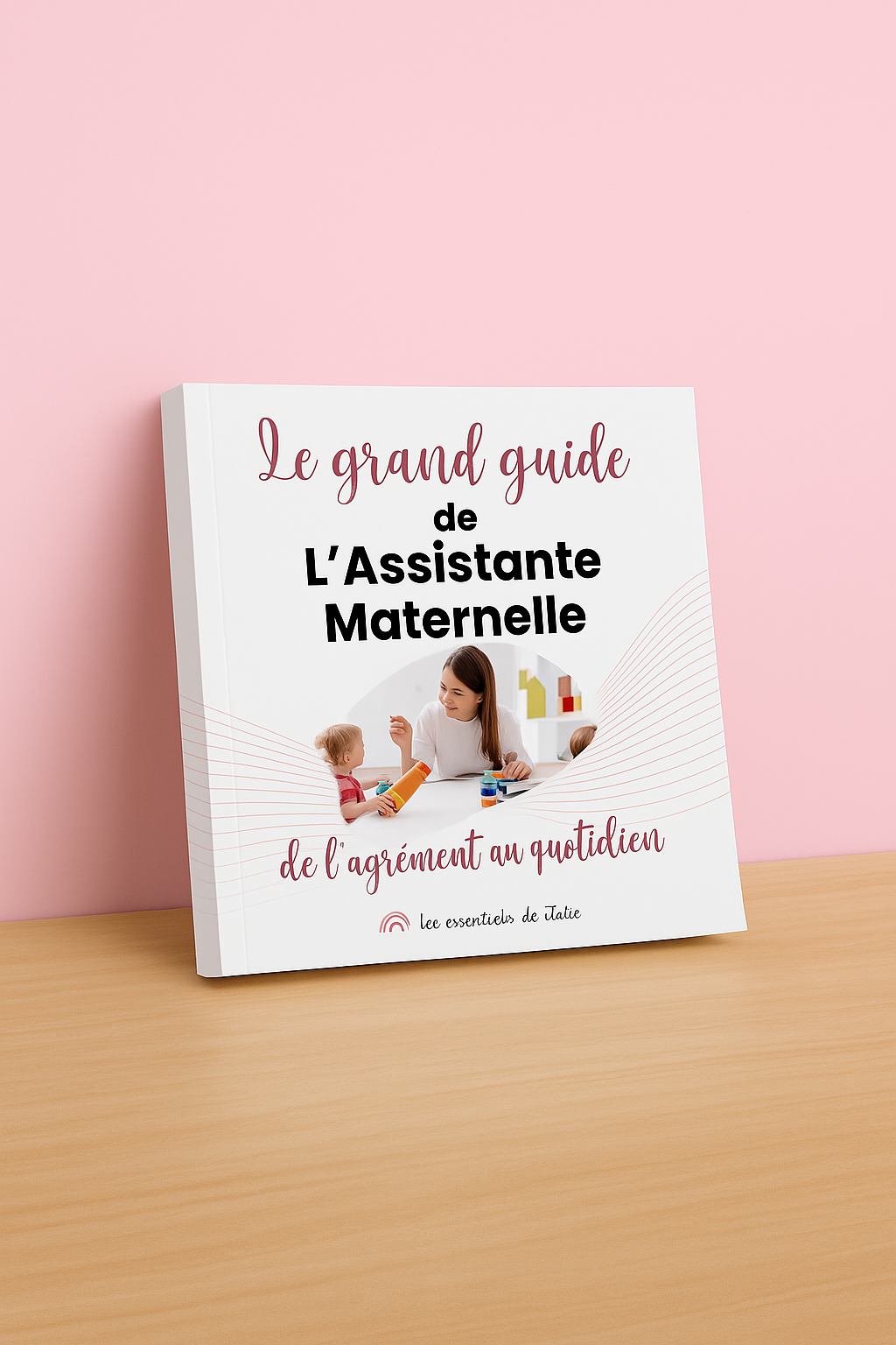 Le Grand Guide de l’Assistante Maternelle – Version Broché Souple 1 Mockup du livre broché souple Le Grand Guide de l’Assistante Maternelle, présenté debout sur un bureau avec fond rose.